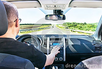 The man is adjusting sound volume in the car stereo (radio). Stock Photo