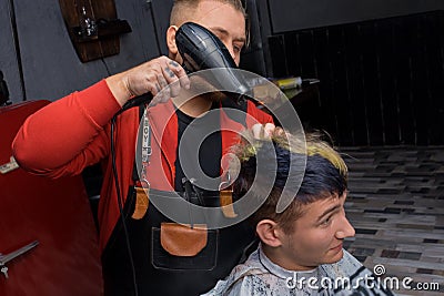 A man, an adult, an experienced, stylish salon worker, blow-drying the hair of a client, a young guy Stock Photo