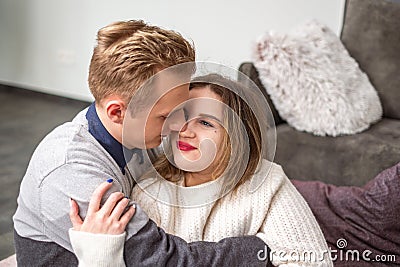 A man affectionately kisses a woman's cheek, their cozy embrace depicting love and comfort, a touching Valentines Stock Photo