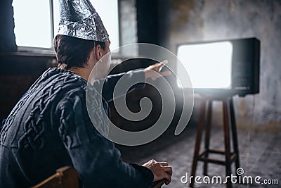 Man in aluminum foil helmet reaches out to the TV Stock Photo