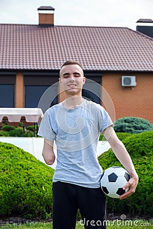 man with amputated arm holds foot on soccer ball while standing on the lawn Stock Photo