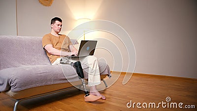 Man amputee with prosthetic leg disability on above knee transfemoral leg prosthesis artificial device using laptop at Stock Photo