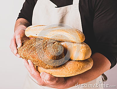 A men in an apron holds various fresh bread loaves with golden crisp in her hands. Homemade alternative bread Stock Photo