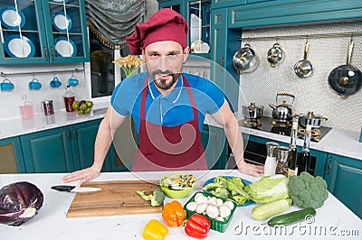 A Man in apron in the kitchen doing salad for vegans. Handsome man cooking at home preparing salad in kitchen. Handsome happy male Stock Photo