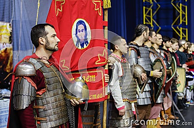 Man in the armor of an ancient Russian warrior near the red banner with the image of Christ the Savior Editorial Stock Photo