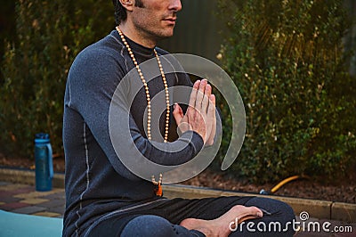 Close-up man athlete, yogi sitting folded palms together, practicing yoga outdoors. Prayer, gratitude. Spiritual growth Stock Photo