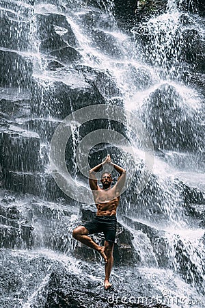A man of athletic build does yoga. Healthy lifestyle. The concentration of the body. A man does yoga at a waterfall. Stock Photo