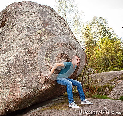 Man with backpack pushing a huge stone Stock Photo