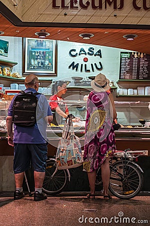 Man with a backpack and a woman with a bicycle doing the shopping in the market at the legume stand Editorial Stock Photo