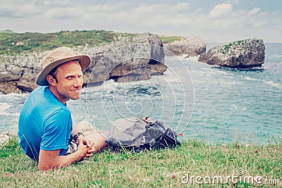 Man backpacker traveler rests on the rocky sea side, looks in ca Stock Photo