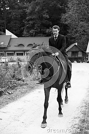 Man in balck suit rides a horse along the road Stock Photo