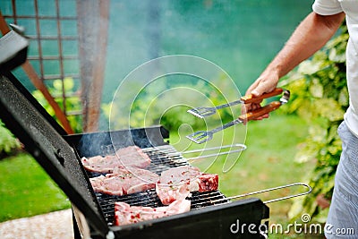 Man at barbecue grill preparing meat for a garden party Stock Photo