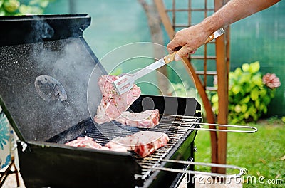 Man at a barbecue grill preparing meat for a garden party Stock Photo