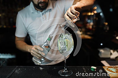 Man bartender makes a delicious cocktail with the addition of white wine, ice cubes and apple slices on a dark background Stock Photo