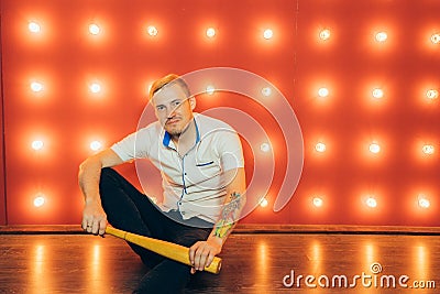 A man with a baseball bat in his hands posing on a red background of spotlights. Stock Photo