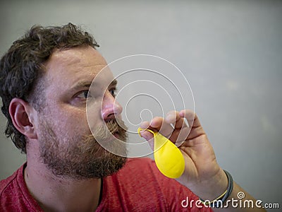 A man with a beard and mustache is preparing to inflate a yellow balloon Stock Photo