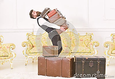 Man with beard and mustache wearing classic suit delivers luggage, luxury white interior background. Macho, elegant Stock Photo