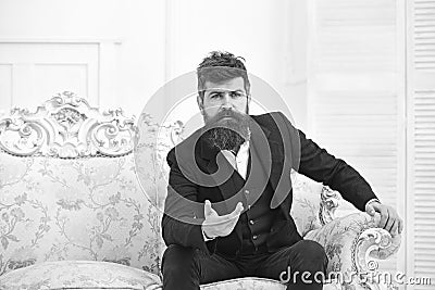 Man with beard and mustache wearing classic suit, sits on old fashioned armchair or sofa. Speaker, wise lecturer concept Stock Photo