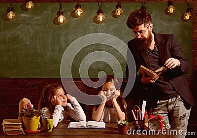 Man with beard teaches schoolgirls, reading book. Bored and tired children listening teacher. Teacher and girls pupils Stock Photo