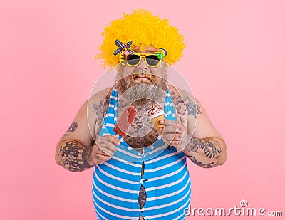 Fat man with beard and wig eats a popsicle and an icecream Stock Photo