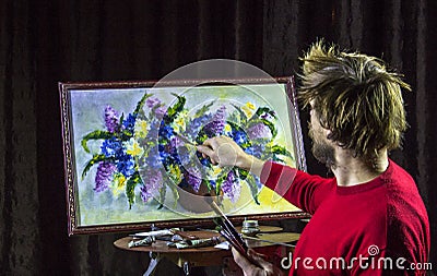 Male bearded artist in a red sweater draws with palette knife painting flowers still life in studio Stock Photo