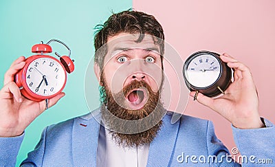Man bearded hipster hold two different clocks. Guy unshaven puzzled face having problems with changing time. Time zone Stock Photo