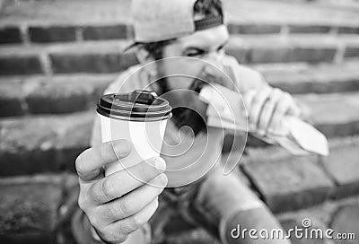 Man bearded shows paper cup drink stairs background. Take coffee with you. Fast food meal for lunch. Hipster bite hot Stock Photo