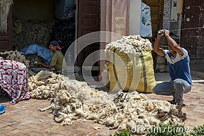 A man beats a pile of wool with a metal bar to remove impurities before the wool is packed into bales in Meknes, Morocco. Editorial Stock Photo