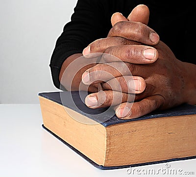 Man with a bible praying with hands clenched together Stock Photo