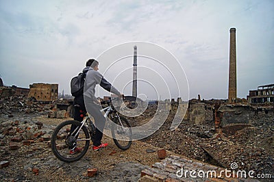 A man on a Bicycle looking down at the ruins of a zinc plant, destroyed brick buildings, the remains of the walls Editorial Stock Photo