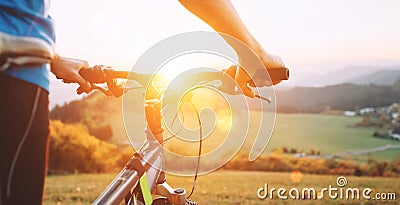 Man with bike stay on the top of hill and enjoying the sunset. Man hands on the bike steering wheel close up image Stock Photo