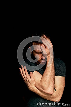 A man on a black background covers his face with his hands. The atmosphere of hopelessness,dejection Stock Photo