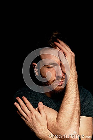 A man on a black background covers his face with his hands. The atmosphere of hopelessness,dejection Stock Photo