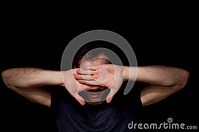 A man on a black background covers his face with his hands. The atmosphere of hopelessness,dejection Stock Photo