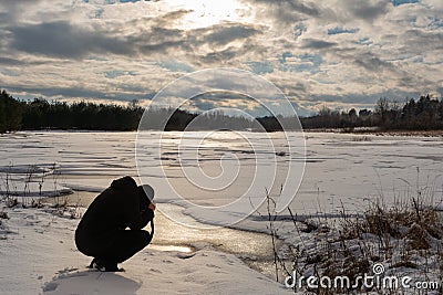 A man in black clothes photographs a landscape near a forest reservoir in early spring during sunset Stock Photo