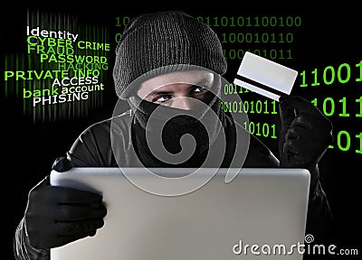 Man in black holding credit card using computer laptop for criminal activity hacking password and private information Stock Photo