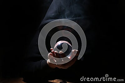 Man in a black hood with cristal ball Stock Photo