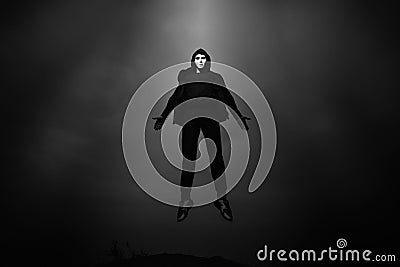 Man in black hoodie wearing white anonymous mask fly up in dark sky. Stock Photo