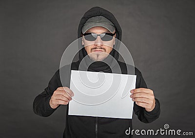 Man in the black hoody with hood wearing sunglasses holding empty sheet of paper Stock Photo