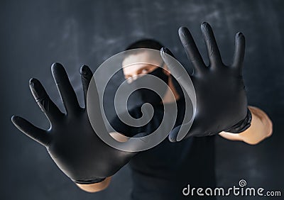 Man in a black mask and medical gloves shows STOP with his hands, on a dark background. The concept of fear and protection against Stock Photo