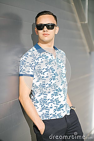 A man in sunglasses stands against a gray wall on a summer day. Stock Photo