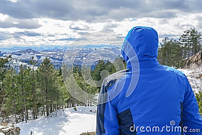 Man with blue jacked sitting and looking on valley and pine tree Stock Photo