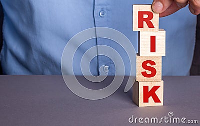A man in a blue shirt composes the word RISK from wooden cubes vertically Stock Photo