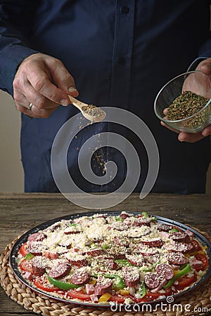 Man in a blue shirt sprinkle with spice pizza from a glass sauser Stock Photo