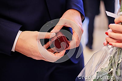 A man in a blue suit holds a small wooden gift box of wedding rings. Stock Photo