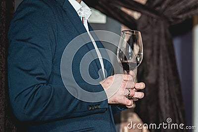 Man in a blue suit with a skin disease holds glass of red wine. people consider the color of the wine and try how it Stock Photo