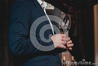 Man in a blue suit with a skin disease holds glass of red wine. people consider the color of the wine and try how it Stock Photo