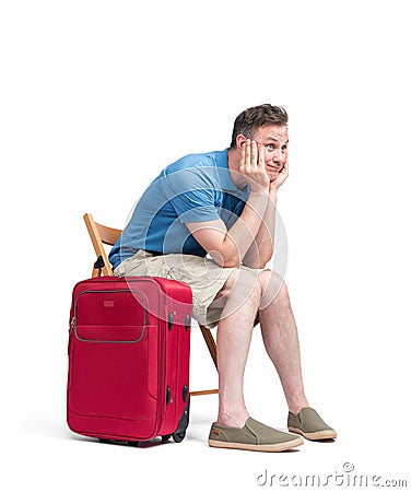 Man in a blue T-shirt and white shorts sits on a chair near a red suitcase, waiting. Isolated on white background Stock Photo