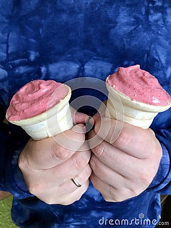 A man in a blue tracksuit holds two servings of ice cream. Ice cream in the horns, has a coral color Stock Photo