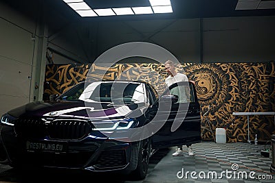 Man with a BMW parked in a Contemporary European Garage, Artistic Mural Adorns Editorial Stock Photo